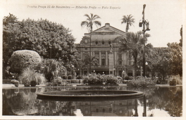 CARTÃO POSTAL - Imagem de 1949 registra a Praça XV de Novembro, no coração de Ribeirão, com o chafariz em primeiro plano e o Theatro Pedro II ao fundo, compondo uma paisagem que sintetiza a elegância urbana do Centro naquele período. Emoldurada por jardins bem cuidados, a cena revela uma cidade que fazia de sua praça central não apenas espaço de convivência, mas também vitrine de sua vida social, comercial e cultural.