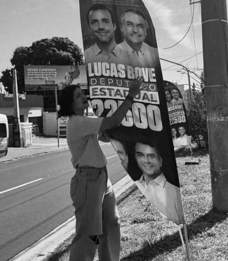 Vereadora Duda Hidalgo ao lado de um banner de Lucas Bove (PL)